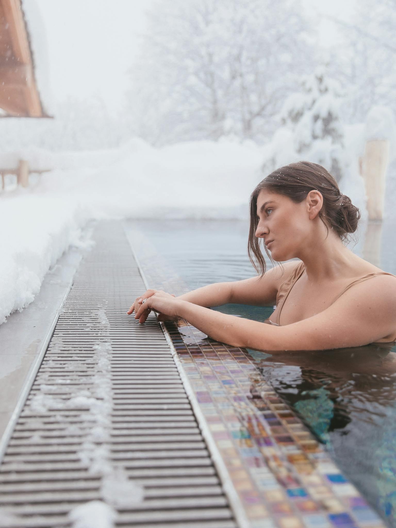 A woman enjoying a peaceful swim in an outdoor heated pool surrounded by snow in winter.